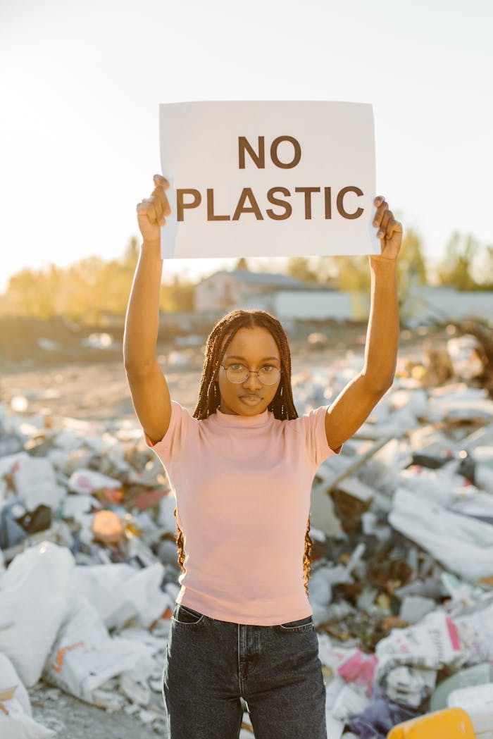 Young woman holding a 'No Plastic' sign at a landfill, raising environmental awareness.
